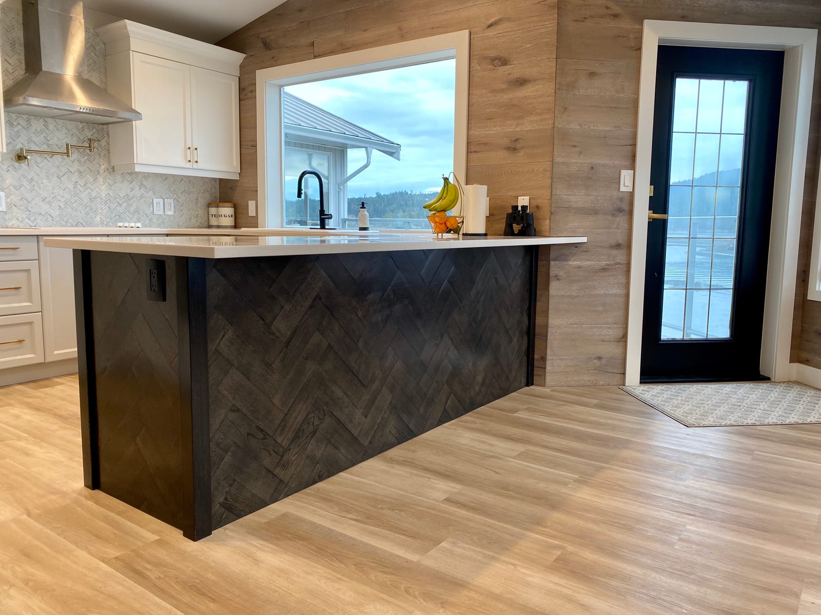 Kitchen island with a dark herringbone wood panel base, white quartz countertop, and a large window overlooking the water