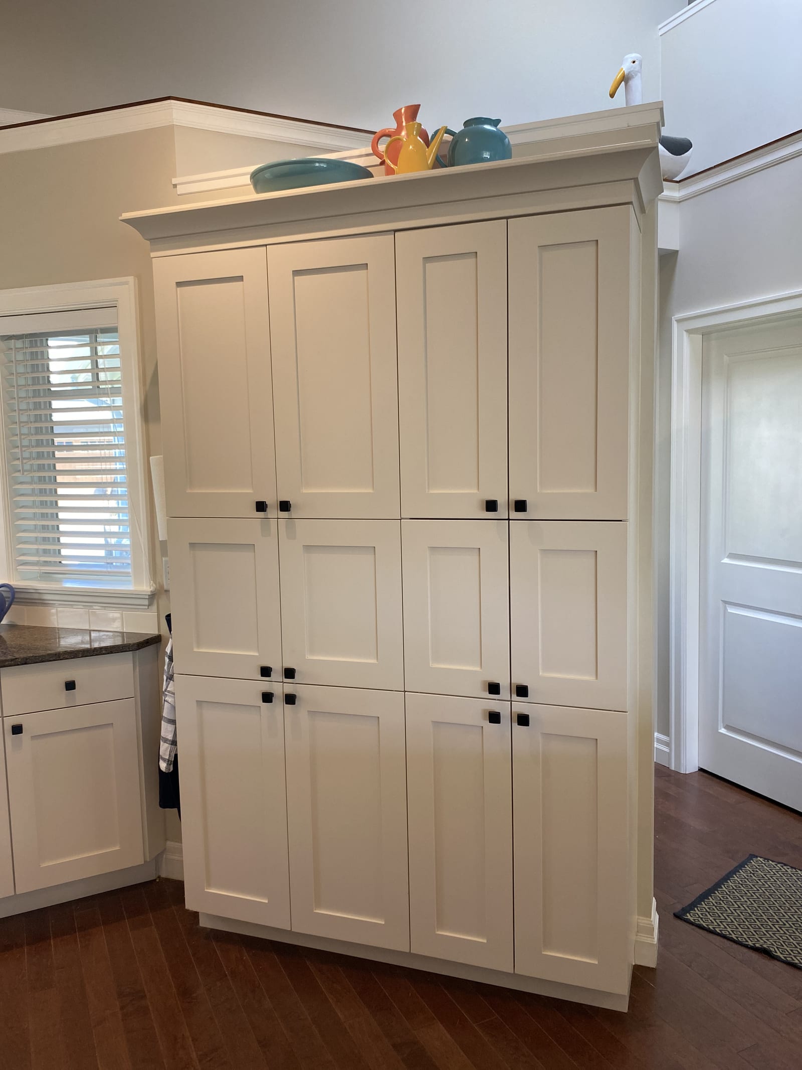 Tall white shaker pantry cabinet with crown moulding and black hardware
