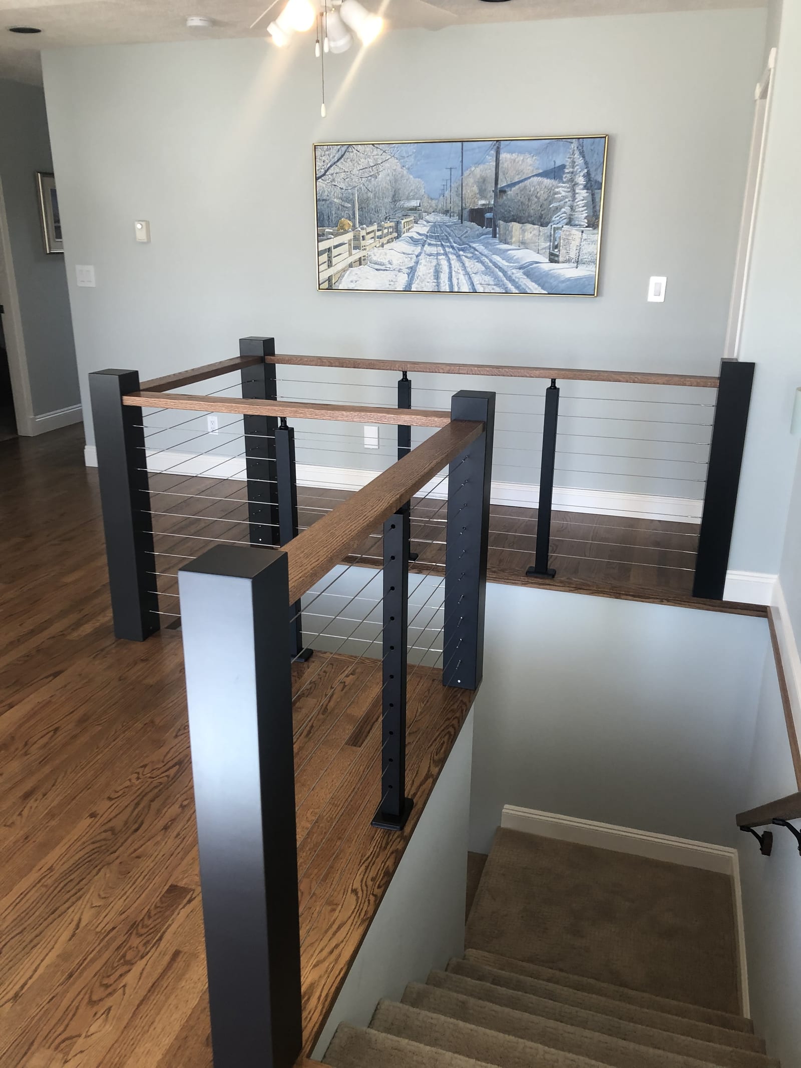 Custom stair railing with a solid wood handrail, black steel posts, and stainless cable infill