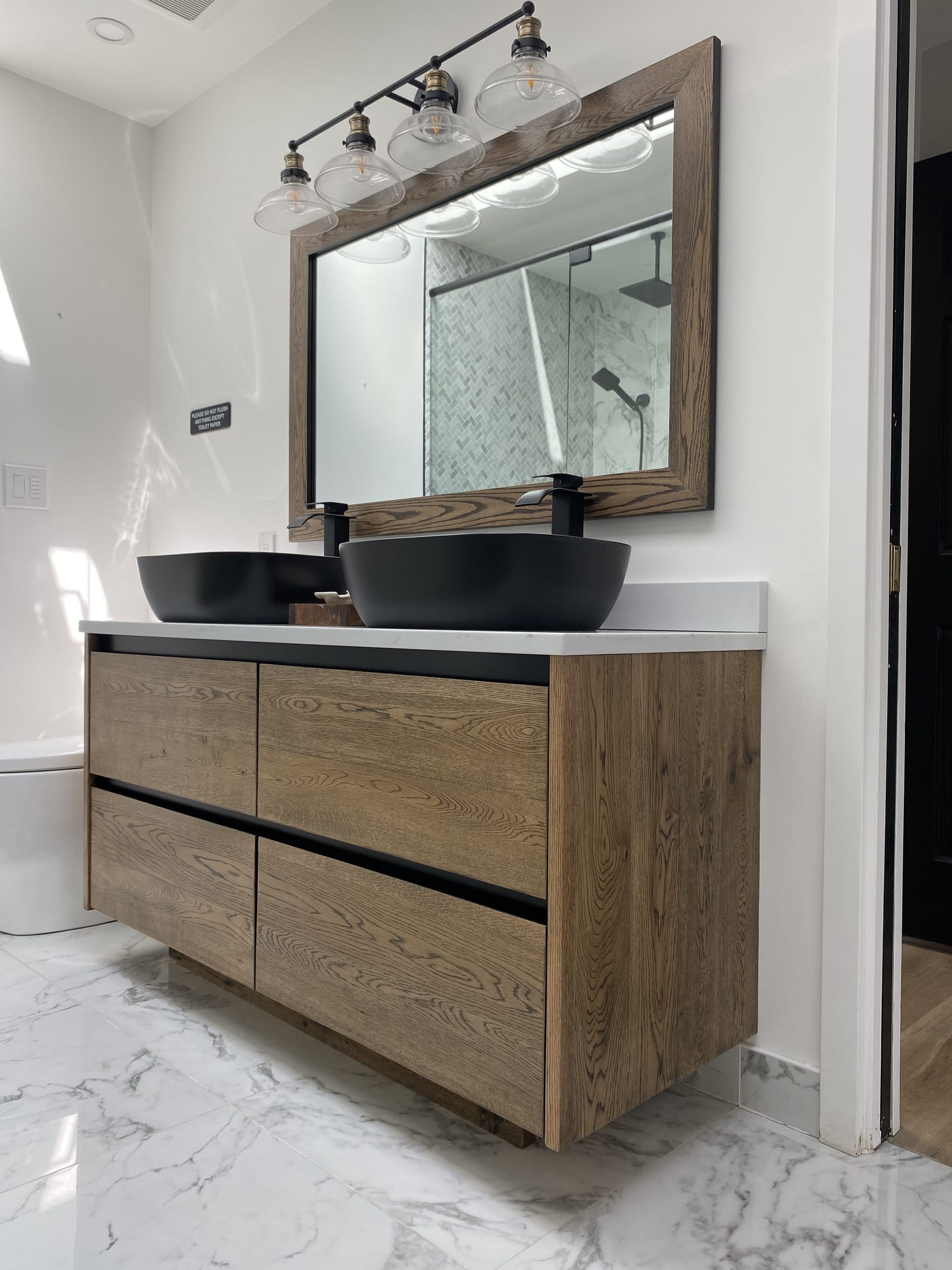 Floating oak vanity with two matte black vessel sinks and a matching wood-framed mirror